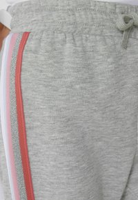 Graue Sweatpants mit einer weichen Textur verfügen über seitliche Streifen in Pink, Weiß und reflektierendem Silber. Der Bund ist mit einem Kordelzug versehen.