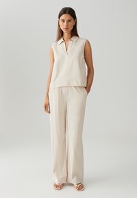 Beige mouwloos topje met een kraag, gecombineerd met losse, bijpassende broek. Gladde textuur, minimalistisch ontwerp en relaxte pasvorm.