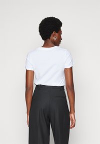 Witte katoenen t-shirt met korte mouwen, gecombineerd met hooggesneden zwarte broek, die een soepele textuur en een getailleerde pasvorm laat zien.