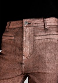Lysbrune denimbukser med en tekstureret overflade, der har en metalknap i taljen og baglommer med minimale sømdetaljer.