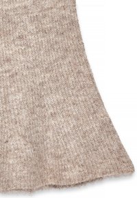Beige stickad tyg med en mjuk textur, med en utsvängd design i fållen. Materialet verkar mysigt och texturerat.