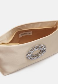 Beige satin clutch-väska med en stor smyckad detalj på framsidan, med en slät yta och dragkedjestängning. Fodrad insida.