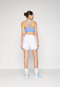 Sutiã desportivo azul claro com um design de costas nadador, combinado com calções atléticos brancos. Modelo a usar meias brancas e ténis azuis.