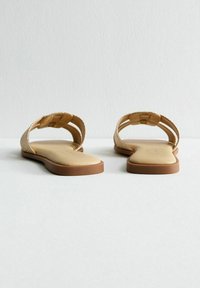 Sandali piatti con cinturini intrecciati color oro e una soletta beige. La suola è marrone chiaro, con una superficie testurizzata per una migliore aderenza.
