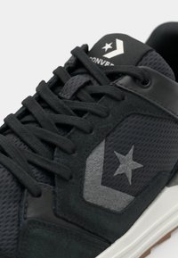 Sort sneakers med en overdel i mesh og ruskind med grå accenter, stjernesymbol og flade snørebånd. Strukturerede paneler og gummisål.