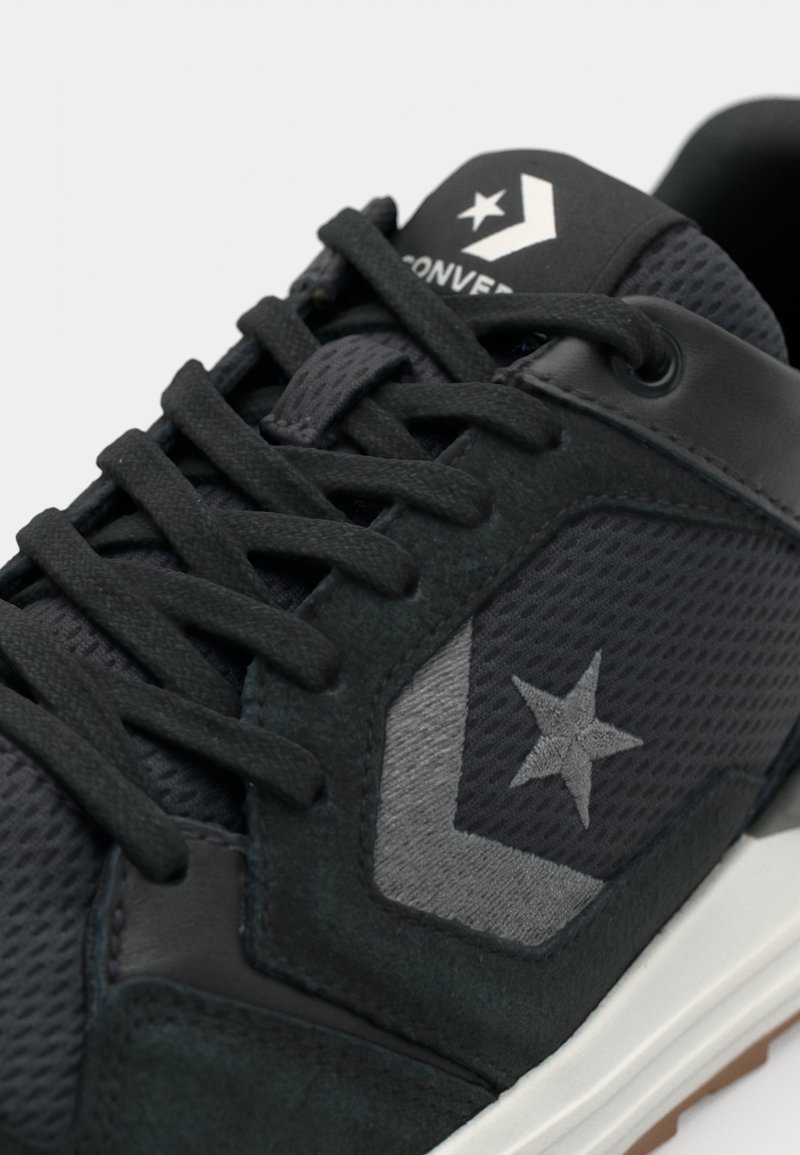 Sneaker nera con superiore in mesh e suede, dettagli grigi, logo a stella e lacci piatti. Pannelli testurizzati e suola in gomma.