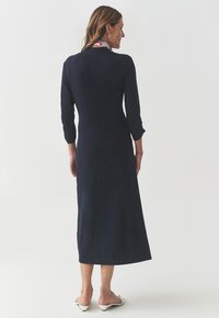 Navy, long-sleeve dress with a fitted bodice and a flowy skirt, made from soft fabric. Features a high neckline and a minimalist design.
