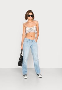 Top cropped branco com bolinhas pretas e bainha com babados, jeans de corte descontraído azul claro, mala preta e ténis pretos com solas brancas.