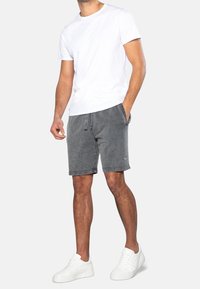 Shorts en coton gris avec une coupe décontractée, dotés d'une taille élastique et de poches latérales, associés à un t-shirt uni à col rond blanc et à des baskets blanches.