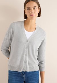 Cardigan grigio chiaro con scollo a V, chiusura con bottoni e maniche a tre quarti. Tessuto a maglia e orlo a coste, abbinato a una blusa bianca.