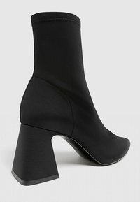 Bottines noires en matériau lisse et extensible, avec un talon épais et une conception élégante et épurée.