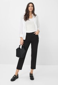Camicia bianca a bottoni sopra una canotta bianca, abbinata a pantaloni neri a tre quarti e una borsa a tracolla nera. Mocassini neri con dettagli dorati.