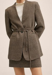 Blazer marrón a cuadros con diseño envolvente, mangas largas y cierre de lazo, combinado con una falda a juego con patrón. Tela texturizada.
