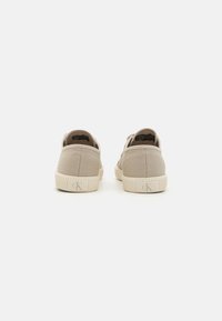 Beige canvas sneakers with a textured upper, contrasting cream rubber sole, and embossed logo on the heel. Simple design, low-profile shape.