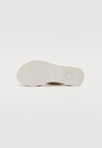 White rubber shoe sole with textured grip pattern, circular indentation, and embossed brand logo. Plain and functional design.