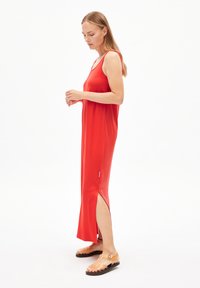 Rode mouwloze maxi-jurk van zachte stof, met zijsplitten en een relaxte pasvorm. Draagt met doorschijnende bandjesandalen.