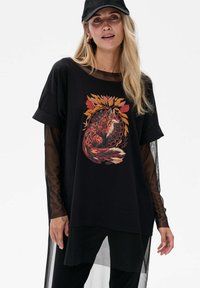 Zwarte oversized t-shirt met een kleurraf fox grafiek omgeven door herfstbladeren, met doorzichtige mesh mouwen en een relaxte pasvorm.