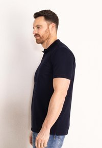 Námořnická polokošile s klasickým límcem, krátkými rukávy a rovný střihem. Má tři knoflíky u krku a nenápadné švy.