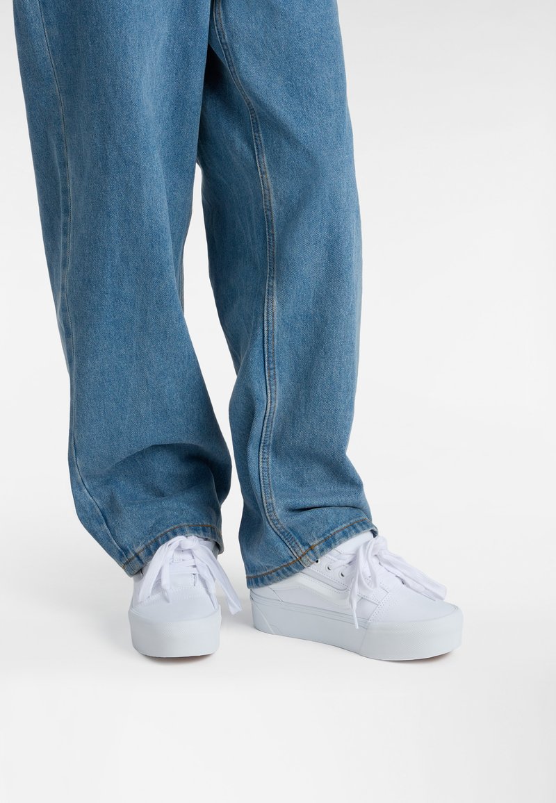 White canvas sneakers with flat sole and rounded toe, paired with light blue, loose-fitting denim jeans featuring a straight cut.