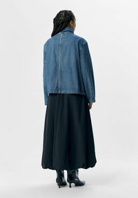 Veste en denim légèrement ajustée, associée à une longue jupe noire à ourlet arrondi, portée avec des bottines noires brillantes.