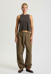 Grauer ärmelloser Crop-Top, lockere olivgrüne Hose mit elastischem Bund und Bündchen, schwarze strukturierte Ballerinas. Einfaches, lässiges Outfit.