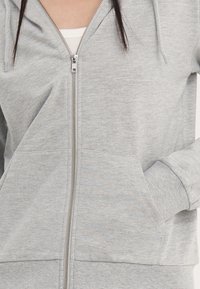 Sweat à capuche zippé gris clair en mélange de coton doux, avec une poche kangourou, des poignets côtelés et une capuche ajustable avec cordon de serrage.