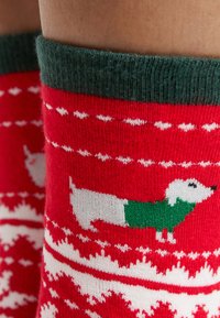 Chaussettes rouges tricotées avec un motif de chien blanc portant une écharpe verte, rehaussées de motifs blancs et d'un revers vert en haut.