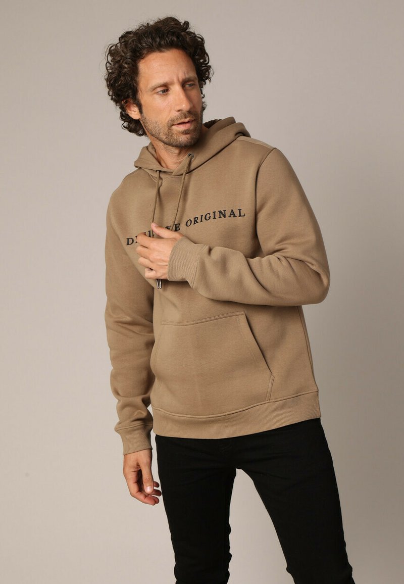 Bruine hoodie met trekkoord, voorzak en zwarte tekst "DEFINE ORIGINAL." Zacht materiaal met ribgebreide manchetten en zoom, ontworpen voor een casual pasvorm.