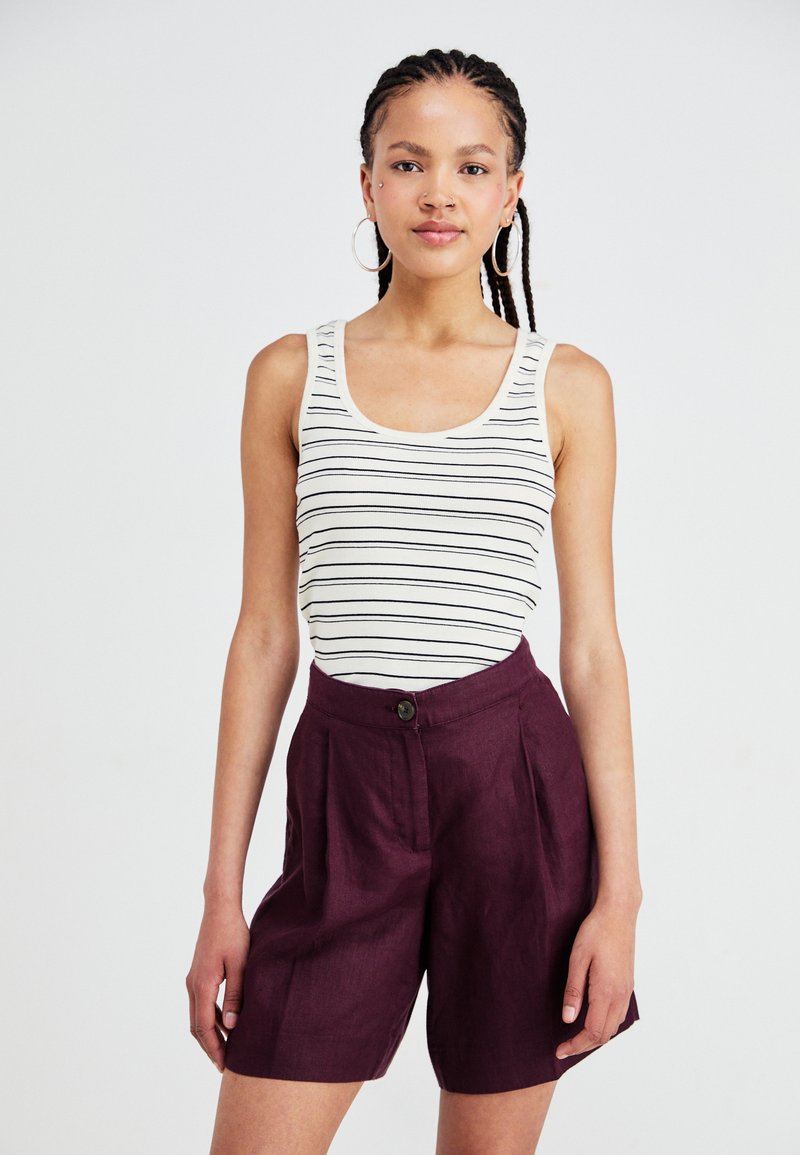 Striped tank top in cream and black, paired with high-waisted plum shorts featuring a button closure and wide-leg cut.