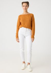 Suéter de punto color óxido con cuello ancho, combinado con jeans blancos de tiro alto y zapatillas blancas. Textura suave; corte casual.