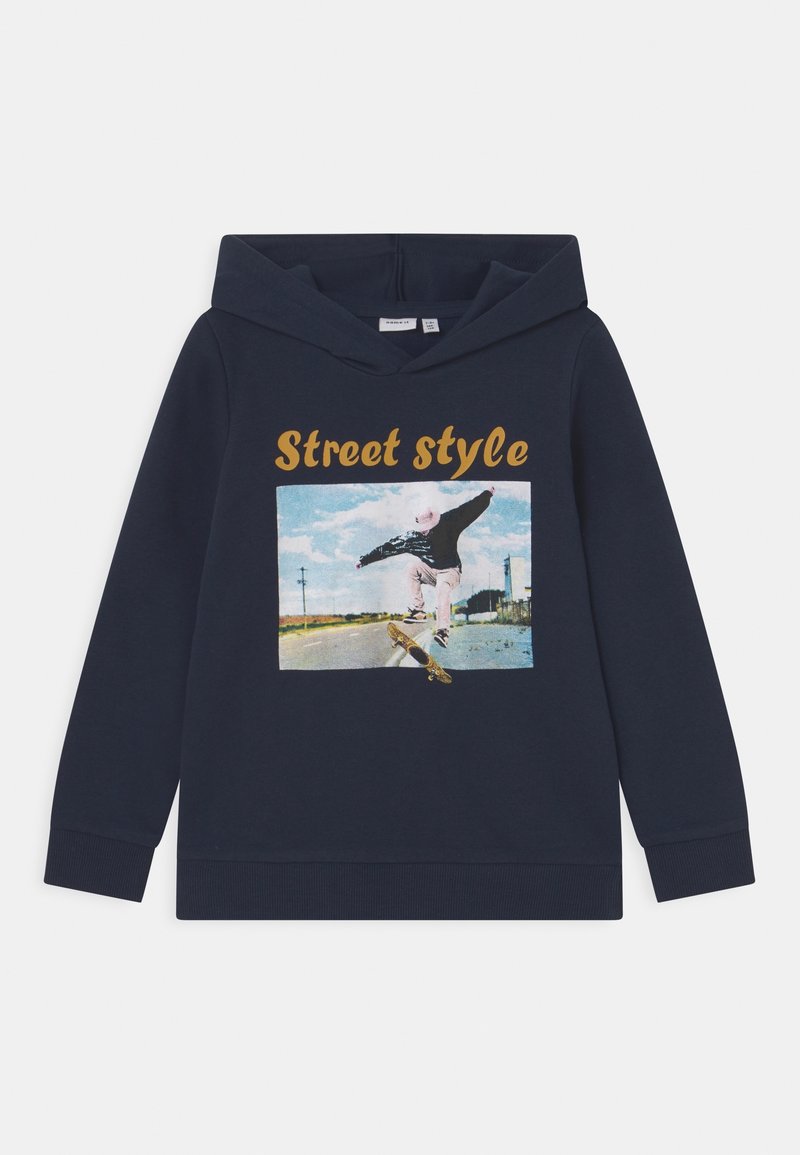 Sweat à capuche bleu marine avec un skateur réalisant un flip sur une route vide sous un ciel bleu, texte "Street style" au-dessus du graphique.