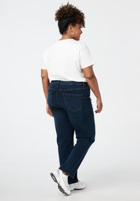 Donkerblauwe denim jeans met een rechte pijp, vijf-pocket ontwerp, zichtbare stiknaad en een klassieke tailleband. Gekoppeld met witte sneakers.