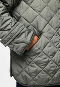 Giacca grigia trapuntata dal design snodato, con tasca e maniche a polsino, realizzata in un materiale morbido e resistente.