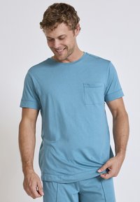 Light blue cotton t-shirt with a round neckline, short sleeves, and a chest pocket. Features contrast stitching on the shoulders.