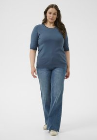 Blaues gestricktes Kurzarmoberteil mit rundem Ausschnitt, kombiniert mit hellblauen Schlagjeans und weißen Turnschuhen. Glatte Textur, lässiger Stil.