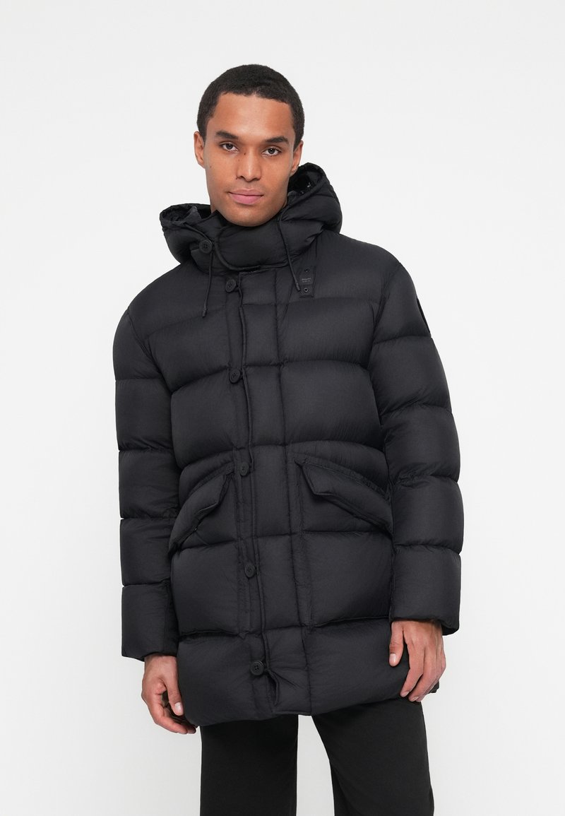 Giubbotto puffer nero con cappuccio, dotato di chiusura con bottoni, due grandi tasche frontali e sezioni trapuntate per l'isolamento.