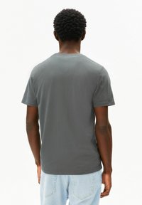 Graues Baumwoll-T-Shirt mit Rundhalsausschnitt und kurzen Ärmeln, von hinten gezeigt. Weiche Textur, lockere Passform, kombiniert mit hellblauen Jeans.