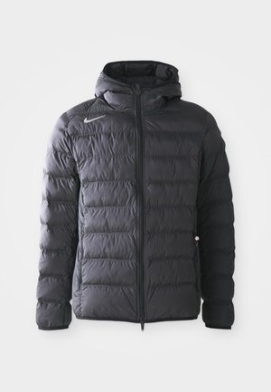 Chaqueta de plumas negra con capucha, diseño acolchado, cierre frontal con cremallera y un pequeño logo reflectante en el lado izquierdo del pecho. Tejido texturizado.