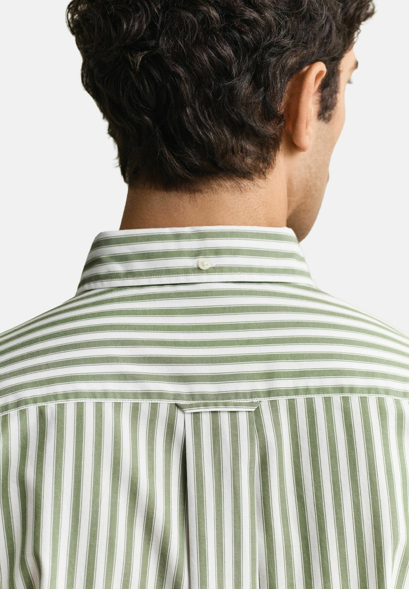 Uomo visto da dietro che indossa una camicia a bottoni verde e bianca a righe verticali con un dettaglio di bottone sul colletto posteriore.