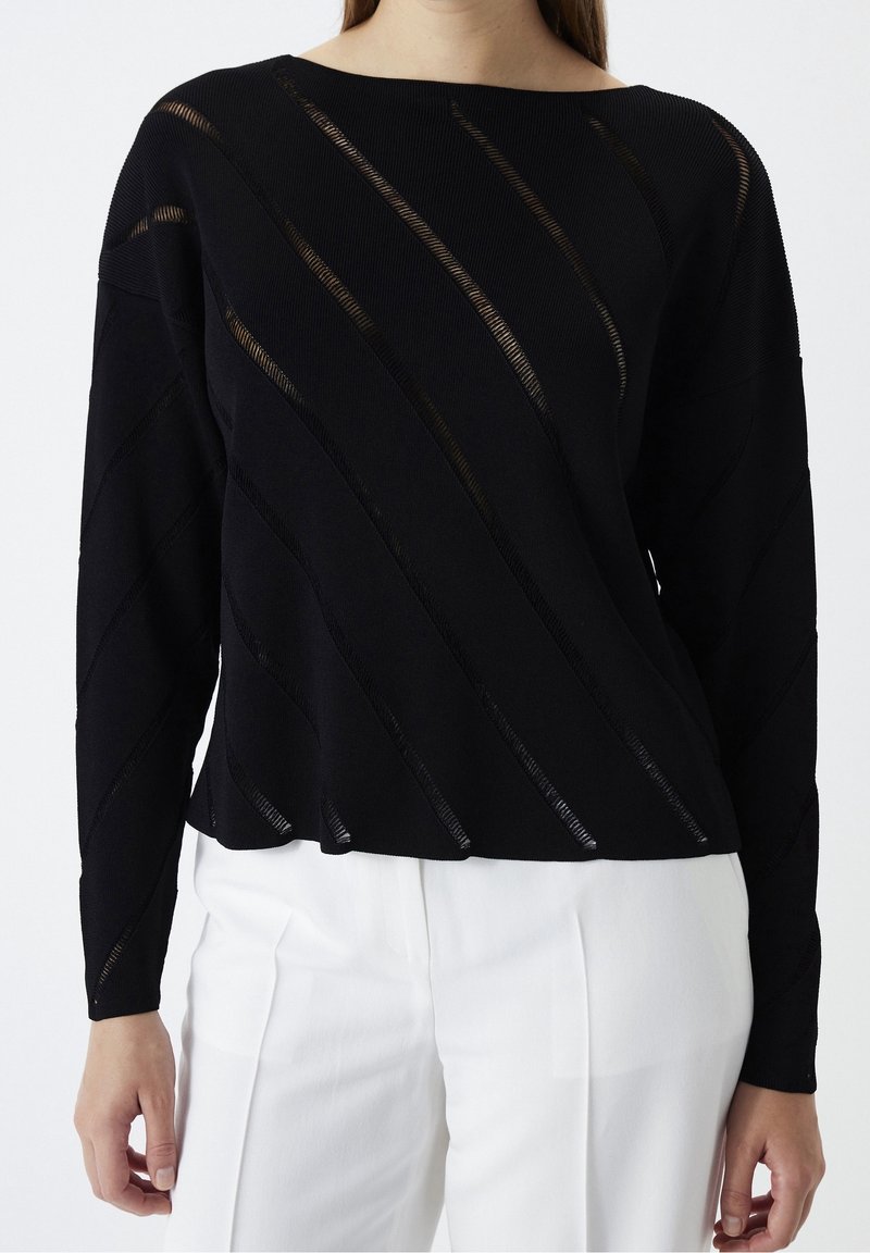 Czarny longsleeve z diagonalnymi wycięciami i fakturowanym materiałem, w połączeniu z białymi spodniami w szerokim kroju. Prosty, luźny fason.