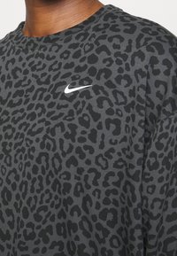 Primer plano del pecho superior de una persona que lleva una camisa de estampado de leopardo en gris oscuro y negro, con un logo de Nike blanco en el lado izquierdo.