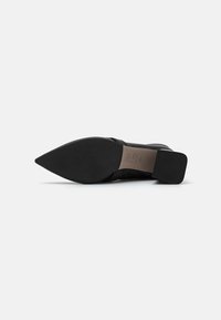 Chaussure noire à bout pointu avec un upper en cuir lisse, un talon plat et une semelle en caoutchouc texturée. Présente un branding minimal sur la semelle intérieure.