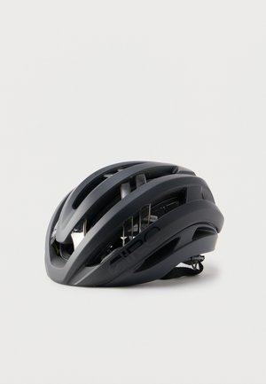 Casco da bicicletta aerodinamico nero con molteplici fessure di ventilazione e cinturino regolabile posato su una superficie bianca.