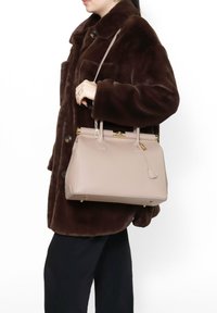 Borsa strutturata in morbida pelle beige chiaro; manici superiori, dettagli in hardware dorato e base piatta con piedini protettivi.