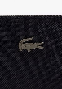 Tela negra texturizada con un logotipo metálico de cocodrilo. El logotipo está detallado con manchas y tiene un diseño de boca abierta, creando un contraste.