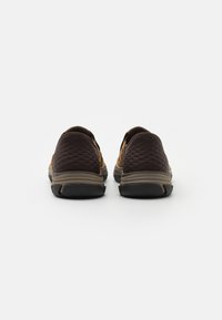 Pantofi slip-on maro și bej, cu o suprafață texturată, toc rotund și talpă din cauciuc negru cu un model subtil.