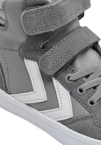 Szary trampki za kostkę wykonany z mieszanki zamszu i skóry, z paskami na rzep, białymi geometrycznymi akcentami oraz fakturowanymi sznurówkami na białej podeszwie.