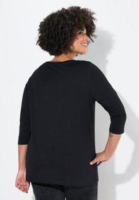 Haut noir léger à manches trois quarts avec une coupe décontractée et un col arrondi, offrant un tissu lisse et un minimalisme dans les détails.