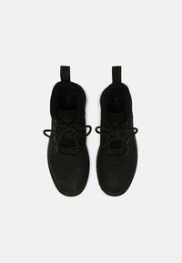 Zapatos negros con parte superior de piel texturizada, cierre de cordones y lengüetas en el talón. Cuenta con un forro suave y suelas planas.