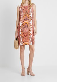 Ärmelloses Kleid mit einem bunten, ornamentalen Muster in Orange, Pink und Lila. Aus leichtem Stoff, knielang mit einem lockeren Schnitt.